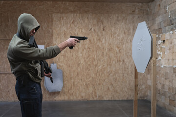 A man in a hooded sweater is engaged in tactical shooting with a pistol g19 and ak 12 rifle at a shooting range.