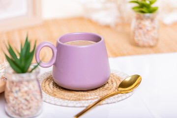 An enchanting sight: a green flower in a glass jar next to a purple coffee mug with a golden spoon amidst boho decor. Perfect for banners, cafes, and floral-themed spaces.