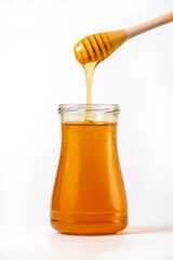 Honey drips from a spoon into a jar on white background