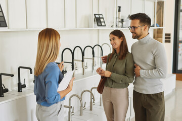 Female shop assistant helping young couple choose new kitchen faucet