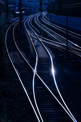 Glistening rails of a main railway line from Hagen to Siegen, Germany. Parallel tracks, switches, catenary and signals seen from bridge at dusk. Blue hour twilight atmosphere with contrasting 