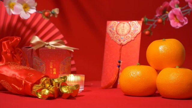 Chinese Lunar New Year background, red theme. gold in silk bag, red gift box with golden bow, paper fan, Tae Eia envelope (red envelope), orange, plum blossom branch, candle and shadow of foliage sway