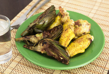 Cooked fried chicken wings and halves artichokes on green plate