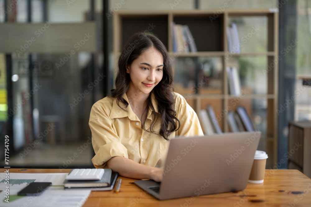 Wall mural attractive asian businesswoman sitting work with laptop and documents at table in office.