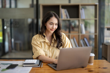 Attractive Asian businesswoman sitting work with laptop and documents at table in office.