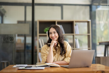 Obraz premium Attractive Asian businesswoman sitting with laptop and documents at table in office, thinking an ideas.
