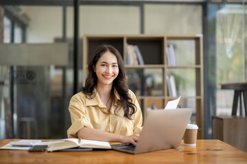 Attractive Asian businesswoman working with laptop and checking documents at table in office.