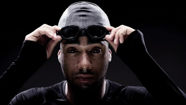 Swimmer, face and goggles, man and athlete with water sport, workout and determination on black background. Challenge, competition and confident with training, exercise and portrait for swimming