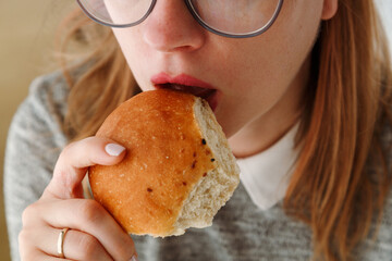 Close up of woman's mouth eating bun, biting bread with hanger, unhealthy snack with carbohydrate....