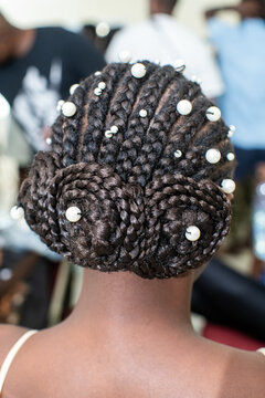 Une main de coiffeuse sur une coiffure africaine avec des tresses et des perles