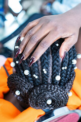 Une main de coiffeuse sur une coiffure africaine avec des tresses et des perles