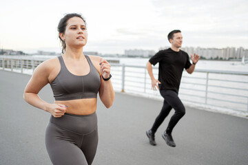 Determined runners training on a waterfront promenade, focus on fitness.