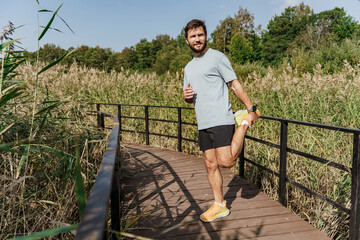 Active man stretching on a wooden bridge in a natural setting, focused on fitness and health.