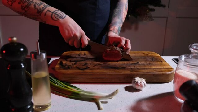 A cook on a wooden board cuts a fried steak into large pieces, close-up