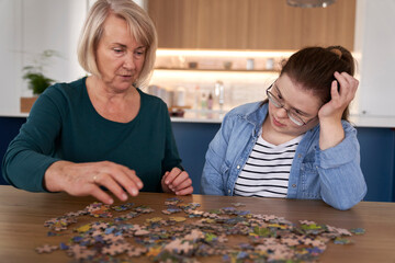 Focus down syndrome woman and her mother assembling puzzles at home