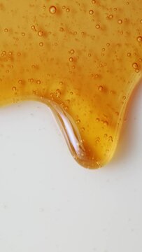 Vertical shot seamless dripping caramel drops sweet sauce or honey clean white background. Close-up macro shot flowing melted yellow orange tasty syrup drip. Confectionery, cooking handmade dessert
