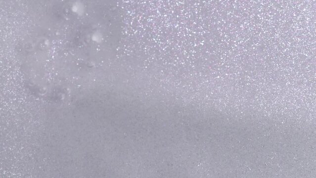 Silver glitter cosmetic product flow down on white background. Liquid drops of lotion with shimmer pouring flow down on canvas. Shiny silver shimmer paint dripping on the white wall