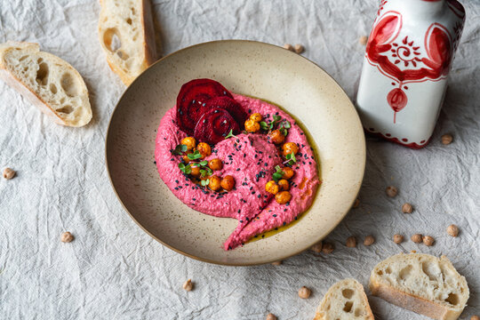 Rote Bete Hummus auf hellem texturierten Teller mit Kichererbsen Garnitur Leinentuch im Hintergrund Oliven&ouml;l Flasche an der Seite