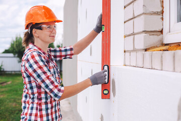 Insulation of the house with polyfoam. The worker is checking with the construction level the...