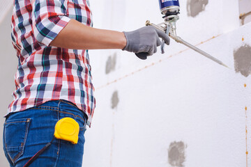 Insulation of the house with polyfoam. worker foaming joints of polystyrene board on the facade.