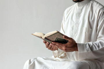 Muslim man dressed in white and praying with quran in hands on white background	
