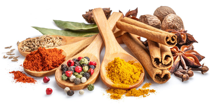 Colorful different seasonings in wooden spoons surrounded with herbs and spices on white background.