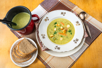 Creamy broccoli soup in plate and pot, sliced bread.