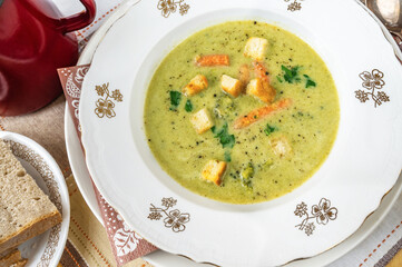 Broccoli soup with sliced fried bread on white plate.