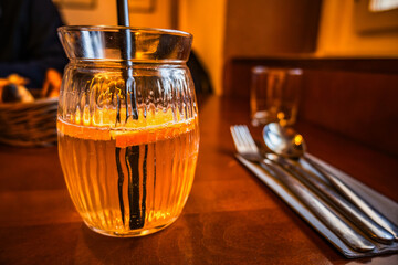 Fruity drink with sliced orange in glass with straw, cutlery, restaurant.
