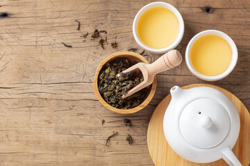 Tea set with tea leaves in bowl and teapot and tea leaves in bowl on wood table background, top view