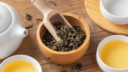 Dried tea leaves in wood bowl closeup with tea set on wooden table