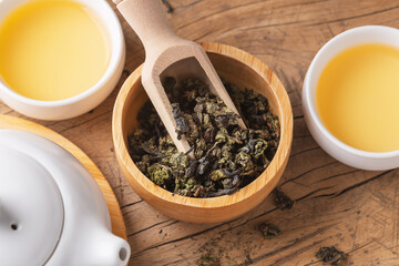 Dried tea leaves in wood bowl with scoop and tea set on wooden table