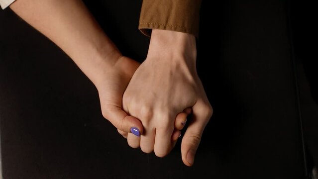 Close-up of man's hand holding woman's hand against a black background. A married couple holding hands comforting each other in a stressful situation. Body language.