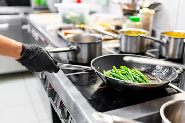 Professional chef cooking asparagus in frying pan on stove in restaurant kitchen