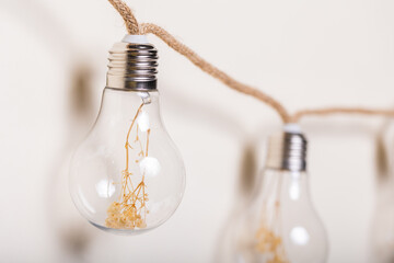 Clusters of delicate, dried golden blossoms encased within transparent light bulbs, suspended...
