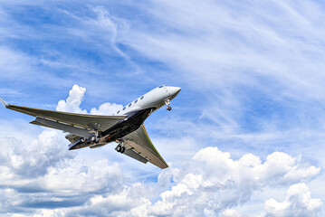 Private business plane flying under blue sky with white clouds
