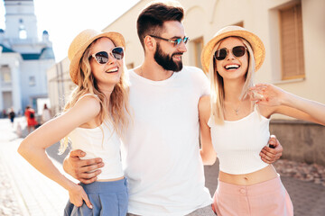 Group of young three stylish friends posing in the street. Fashion man and two cute female dressed in casual summer clothes. Smiling models having fun. Cheerful women and guy outdoors at sunny day