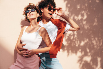 Young smiling beautiful woman and her handsome boyfriend in casual summer clothes. Happy cheerful family. Female having fun. Couple posing in street at sunny day. Near wall at sunset