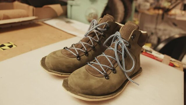 No people shot of unfinished boots made of brown suede on desk in shoemaking workshop