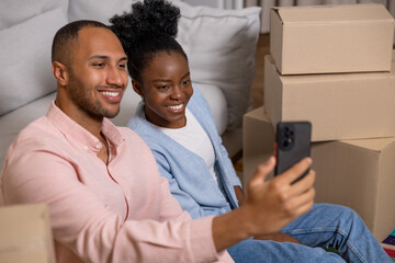 Fototapeta premium Couple taking selfie with smartphone in their new home after relocation surrounded with carton boxes