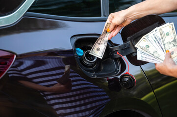 hand of woman that puts money into the tank of car, closeup, concept of expensive fuel, fuel crisis