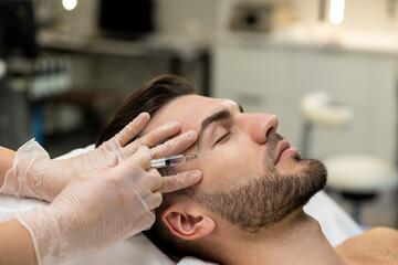 Obraz na płótnie Canvas Dark-haired bearded man having session of mesotherapy in a beauty salon