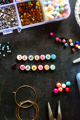 Colorful beads and various jewelry making supplies on dark background. Letter beads spelling JEWELRY MAKING. Top view.
