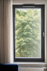 Vertical shot of black closed pvc window with forest view in cozy living room