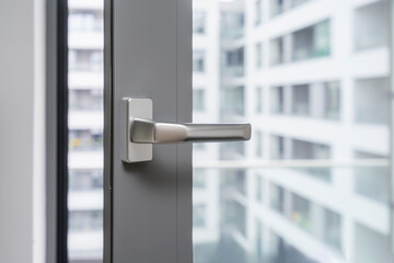 Closeup view of handle of opened gray pvc window against blurred office building background