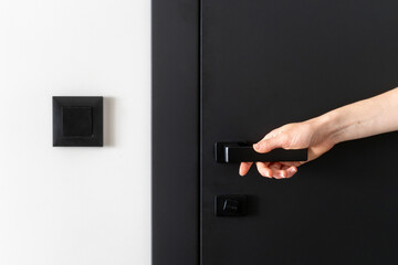 Close up view of woman hand closed modern black door with metal handle