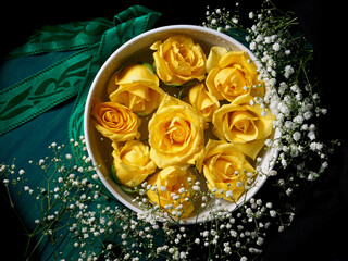 Yellow roses in white bowl on dark green