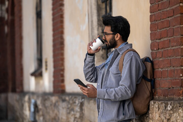 Fototapeta na wymiar Young handsome hindu man standing near the wall with a coffee cup in hand