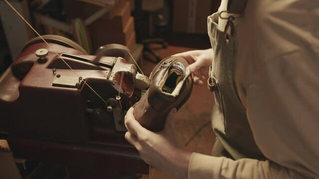 Over the shoulder shot of professional shoemaker working with stitching machine while finishing handmade leather boot in workshop