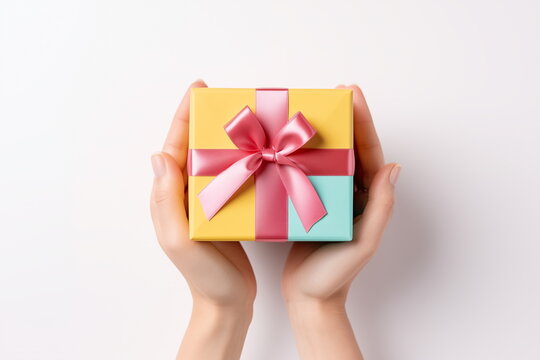 Top view of hands holding craft paper gift box with ribbon bow on isolated pastel blue background. Generated AI.